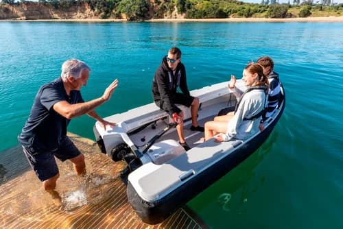 2026 Offshore Cruising Tenders OC300 Inflatable tender viewed from shore, with people boarding and a small outboard motor at the stern.