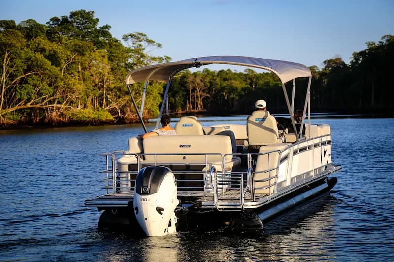 Vision Marine V24 pontoon boat viewed from the stern on a wooded lake, with canopy and outboard motor visible