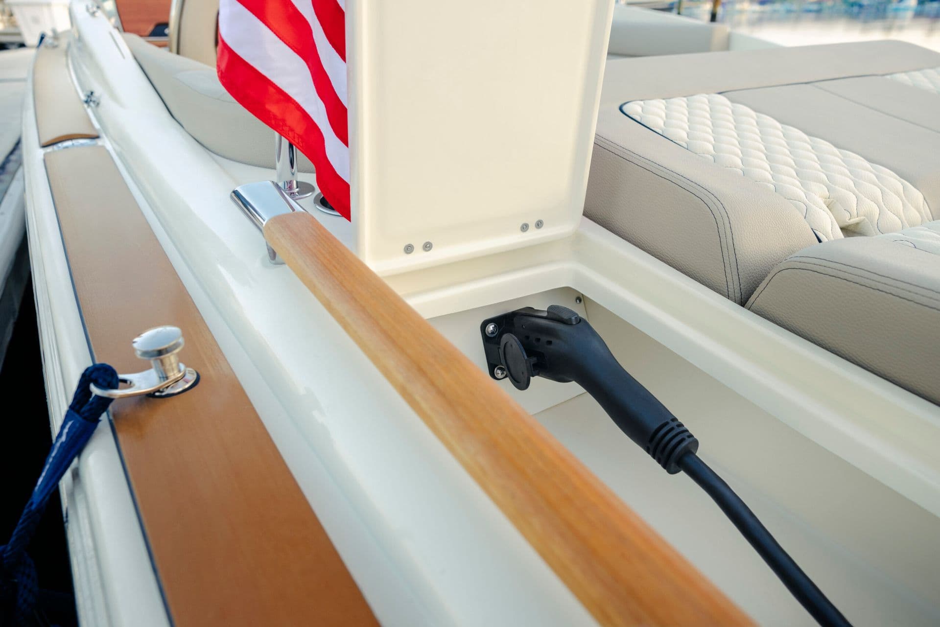 Chris Craft Launch 25 GTe EVOA Electric boat charging cable connected beside the aft seating, with wood trim and an American flag visible.