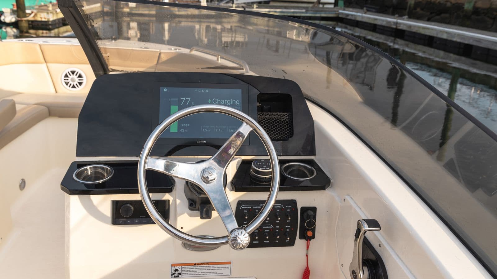Helm of a Scout 215 Dorado showing a steering wheel, Flux Marine digital display, controls, cup holders, and cream-colored seating.