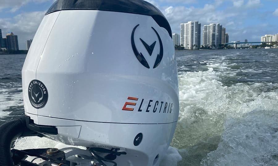 Close-up of a white Vision Marine electric outboard motor powering a boat past high-rise waterfront buildings in background