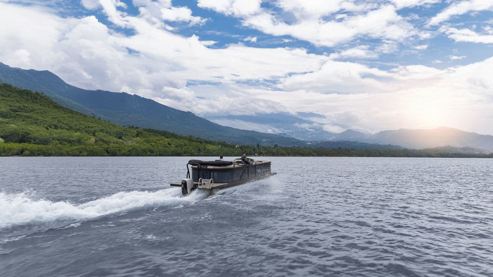 Flagship Discover underway on a lake, viewed from behind, with mountains and clouds in the background