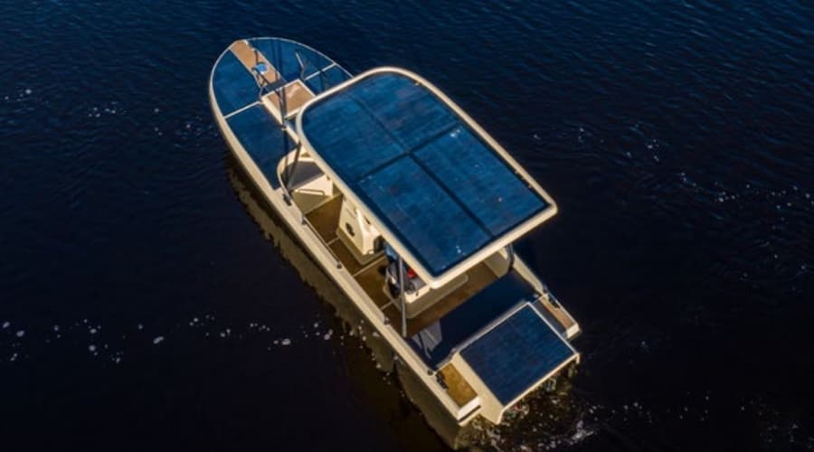 Aerial view of the Elvene Amber electric boat cruising on dark water, with solar panels covering its roof and rear deck.
