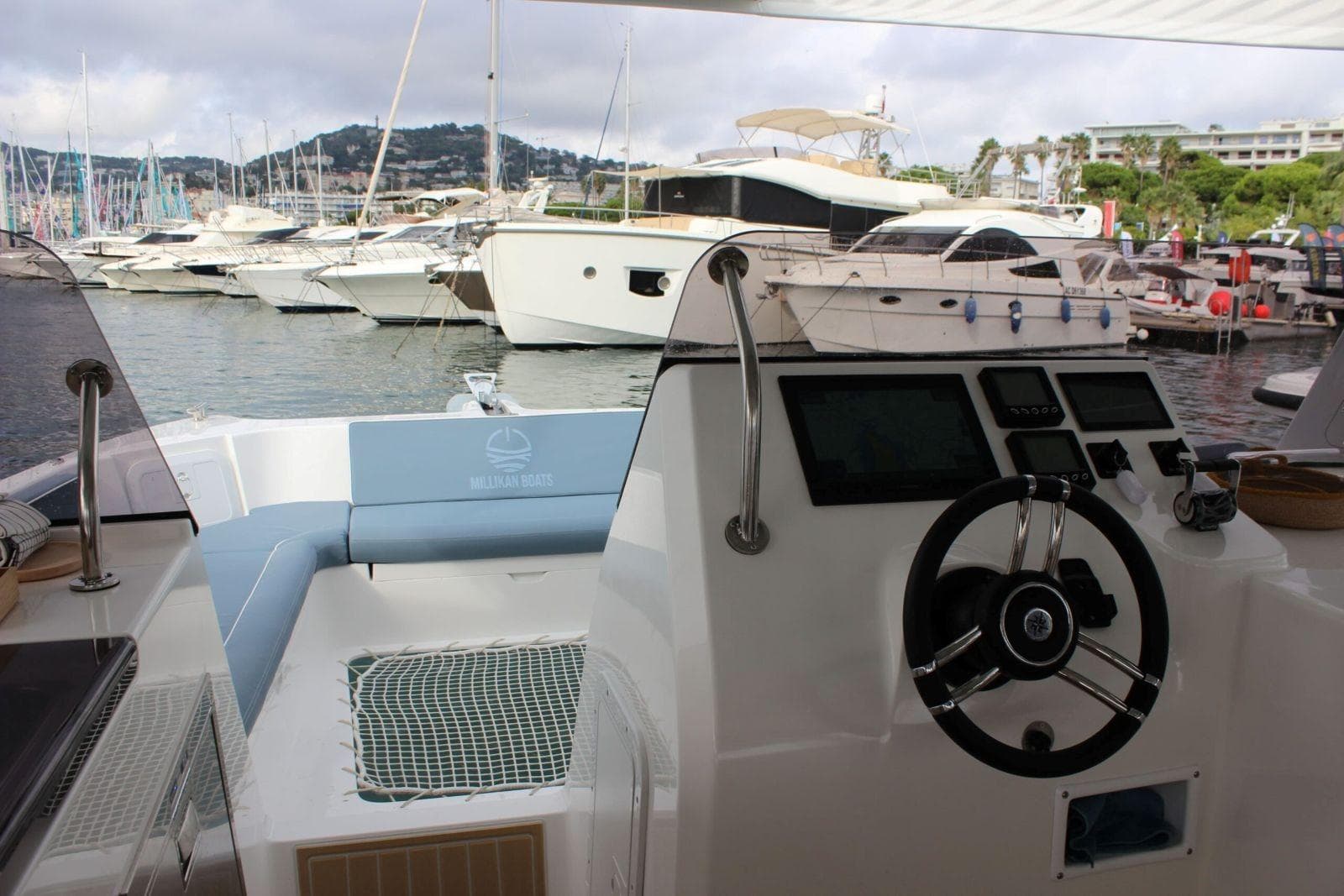 Millikan M10 helm and forward cockpit viewed from aft, with steering wheel, displays, seating, and marina visible.