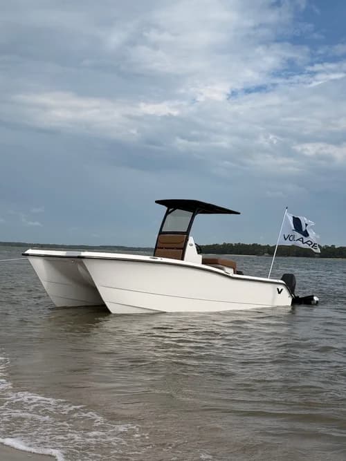 White Volare Artemis 23-style center-console boat floating in calm coastal water, with canopy, outboard motor, and Volare flag.
