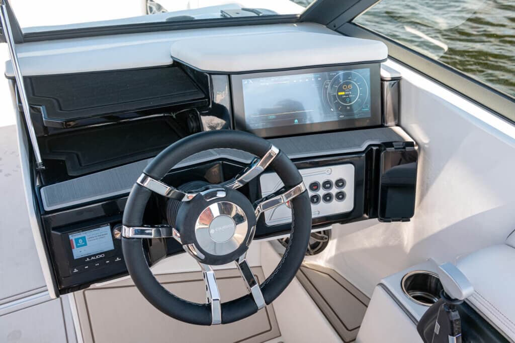 Electric boat helm with steering wheel, digital dashboard display, control panel, and cup holder.