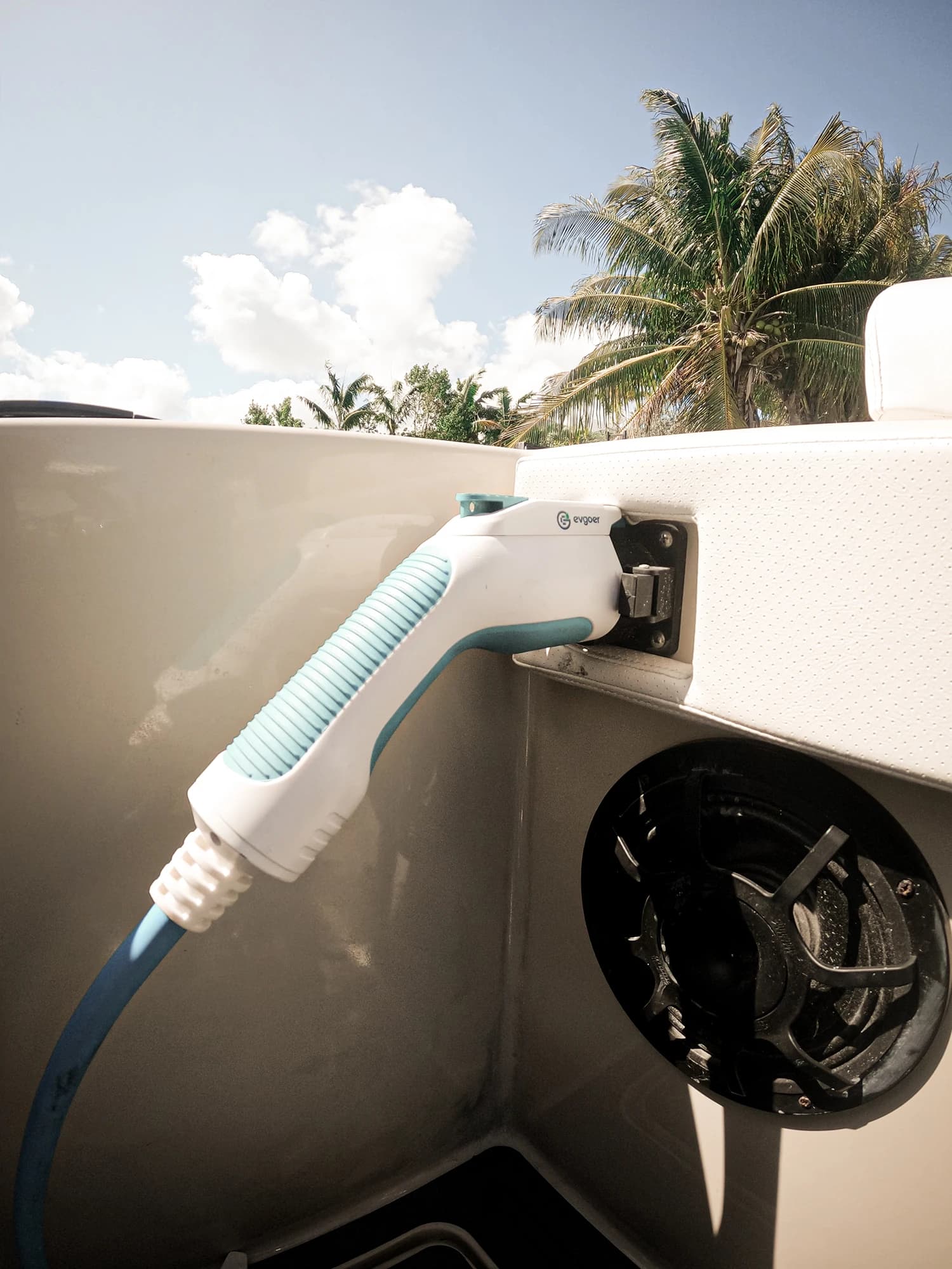 Electric vehicle charging cord plugged into a marine vessel’s charging port, with palm trees visible in the background.