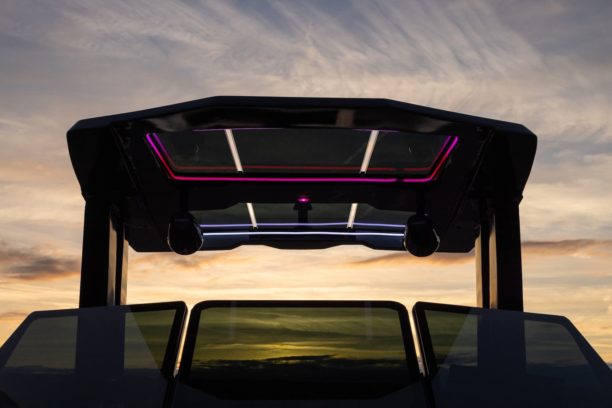 Close-up view from the cockpit of a Voltaic AEW24 electric boat, showing the carbon fiber  T-Top, windshield, and illuminated overhead panel at sunset