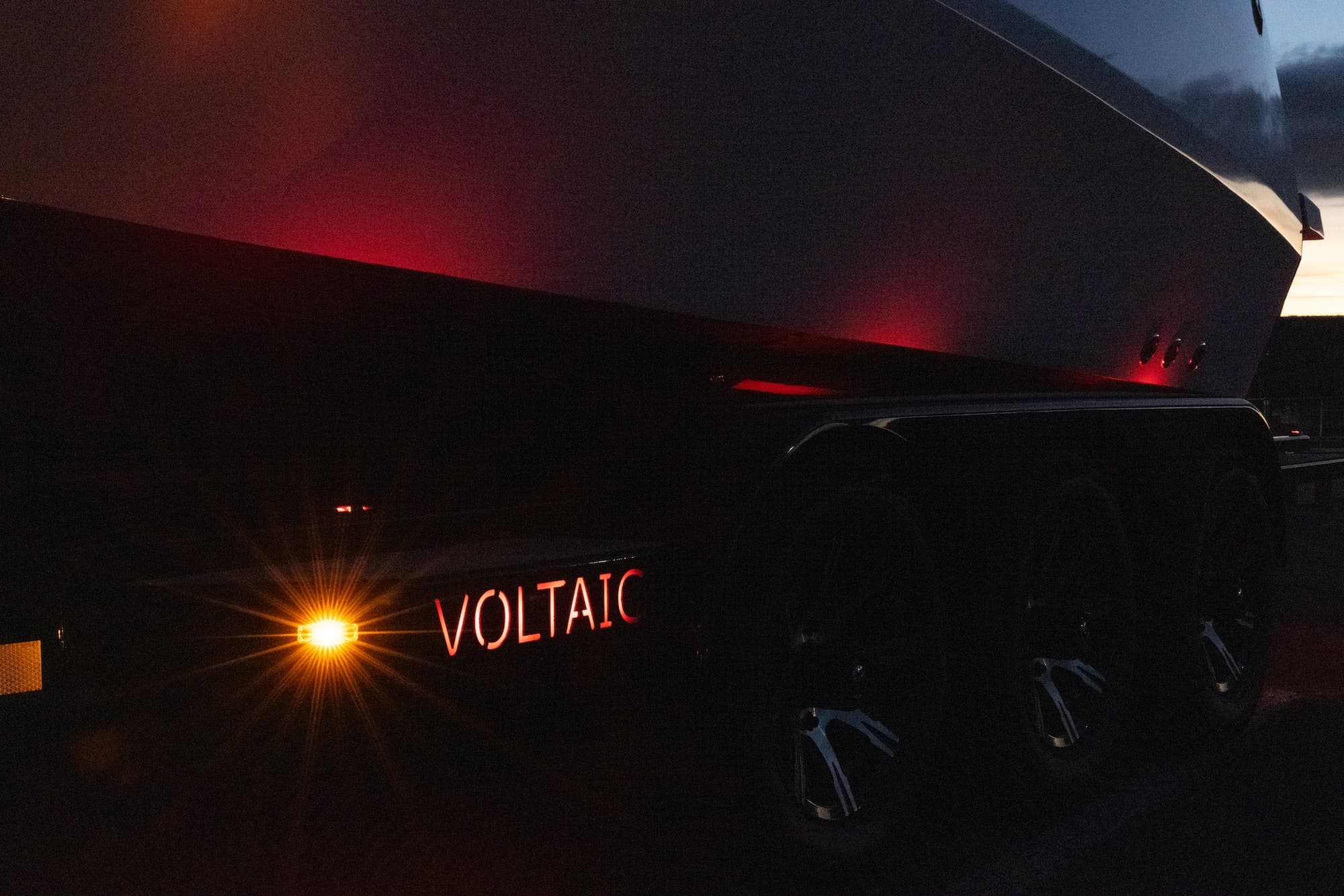 Close-up of a Voltaic electric marine vessel at dusk, showing illuminated branding and red accent lights along the dark hull.