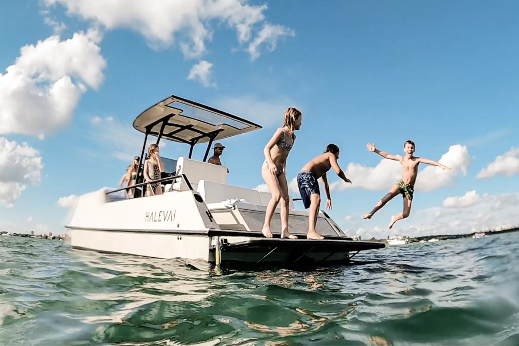 Halevai electric boat with canopy and three passengers on swim platform, one of them is jumping into the water