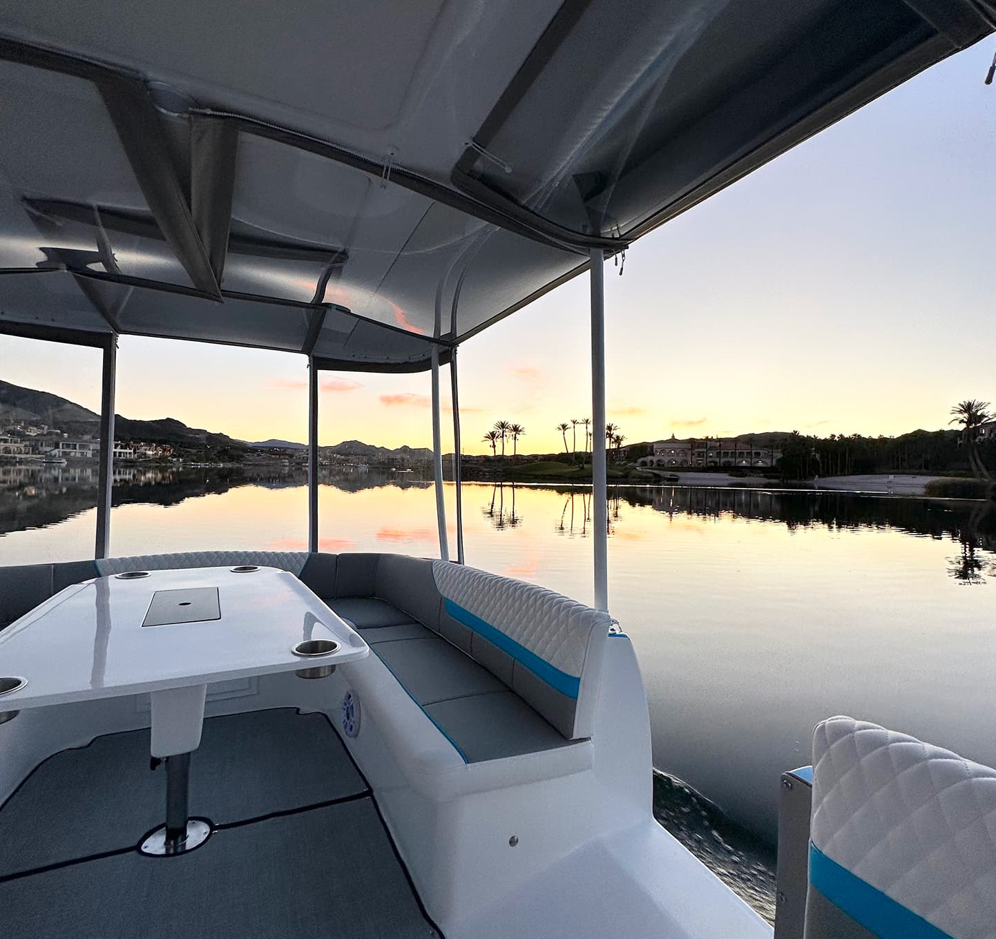 ElectraCraft 162TR interior with canopy, seating, and table  with cupholders overlooking calm waterfront at sunset.