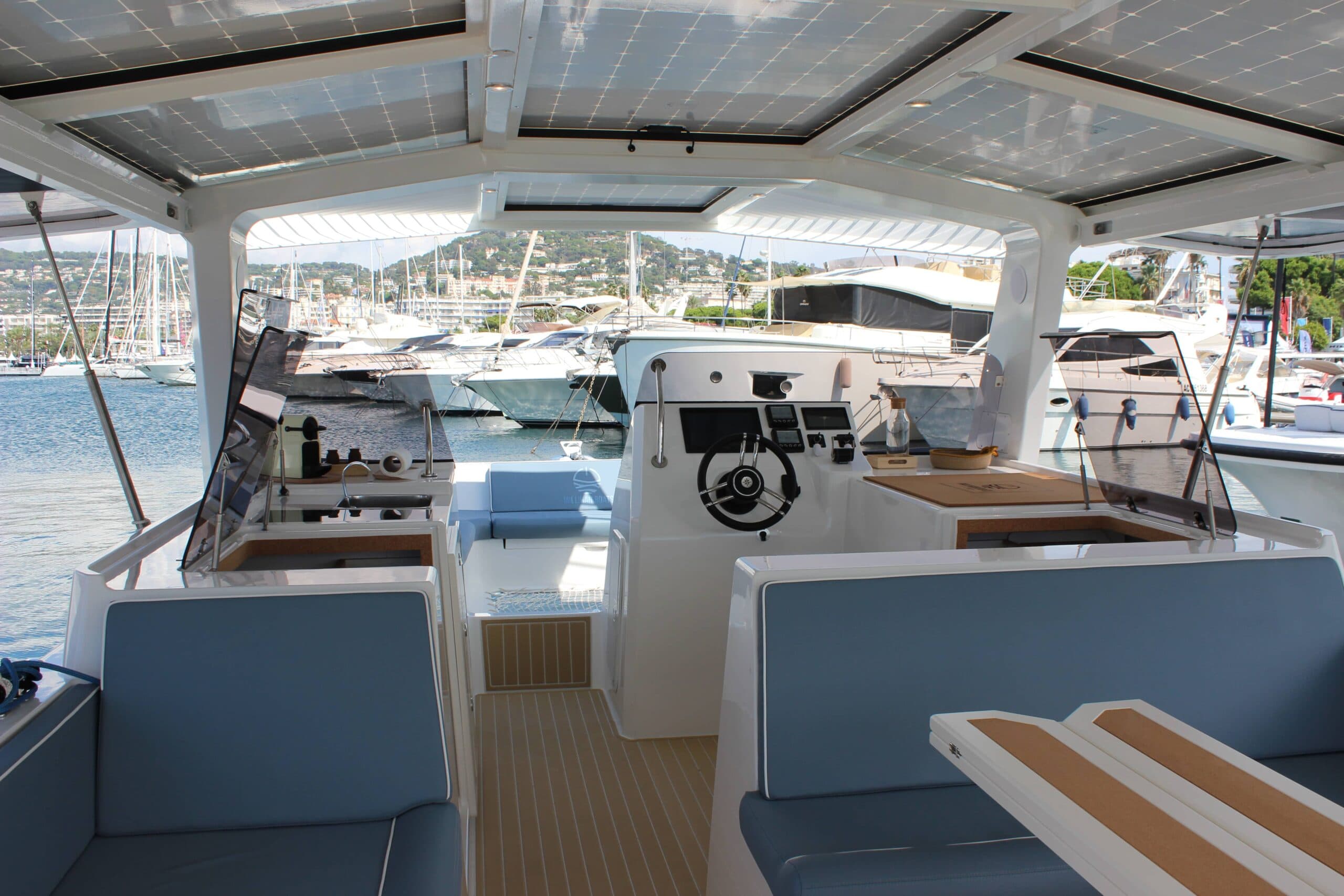 Millikan M10 electric catamaran cockpit with covered helm, cushioned seating, solar-panel roof, and marina views.