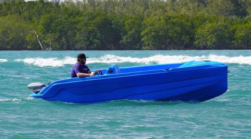 Blue Vision Marine Phantom electric boat cruising on turquoise water, with a person seated at the helm and a forested shoreline behind.