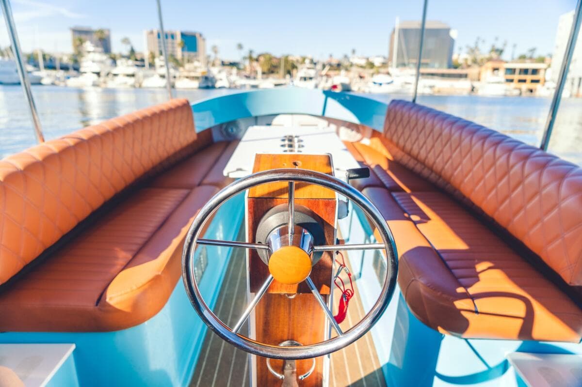 Turquoise boat (Vision Marine Fantail) cockpit with a wooden helm, stainless steel steering wheel, and quilted brown/orange bench seating on a marina.