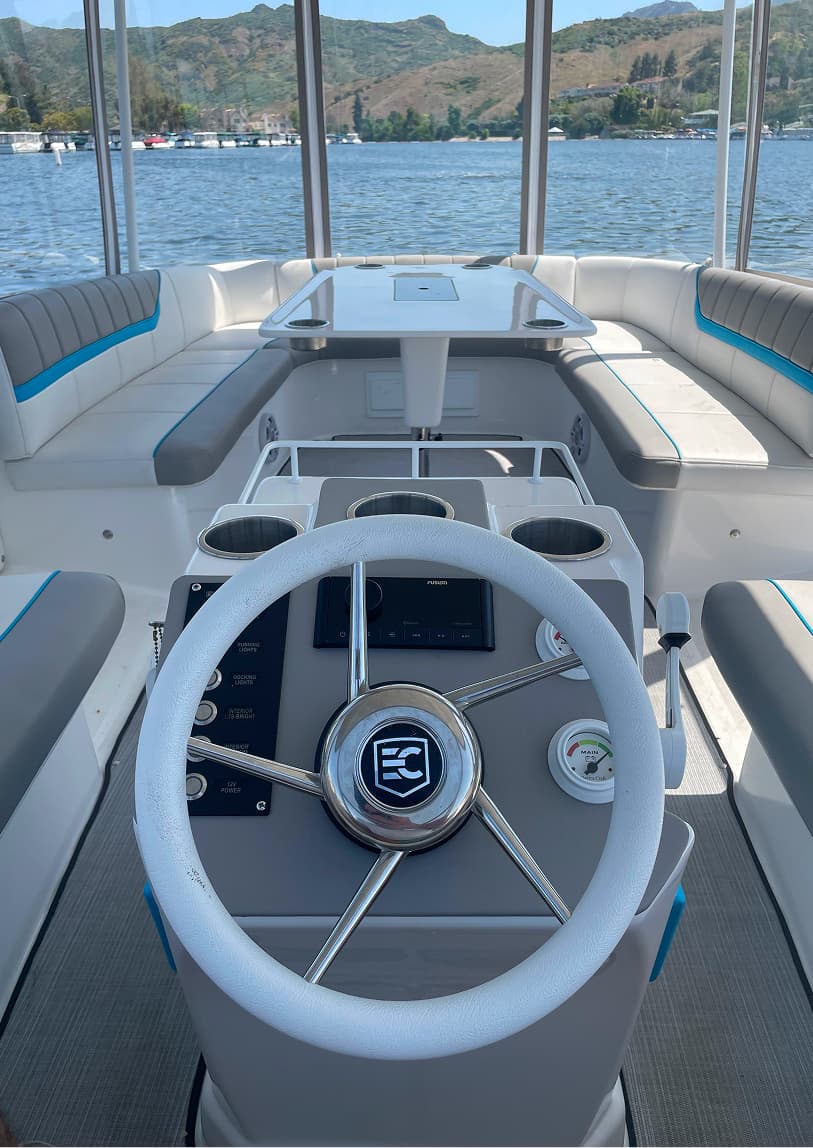 ElectraCraft 162TR boat interior with helm, steering wheel, seating with blue accents, folding table, and lake and mountains visible beyond.