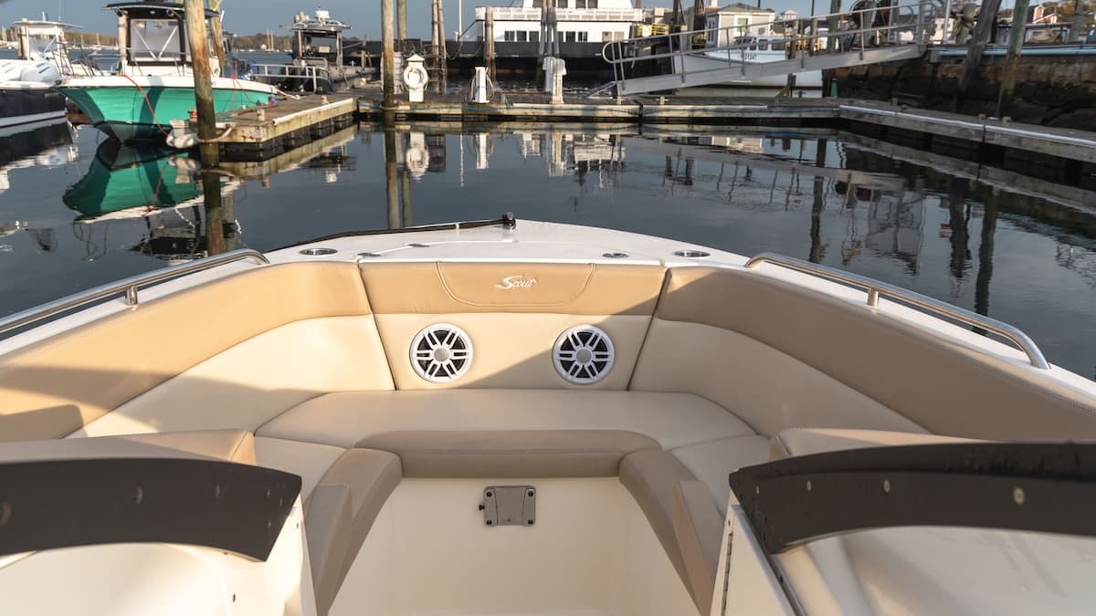 Scout 215 Dorado bow seating with tan cushions and twin speakers, viewed from the helm at a marina.