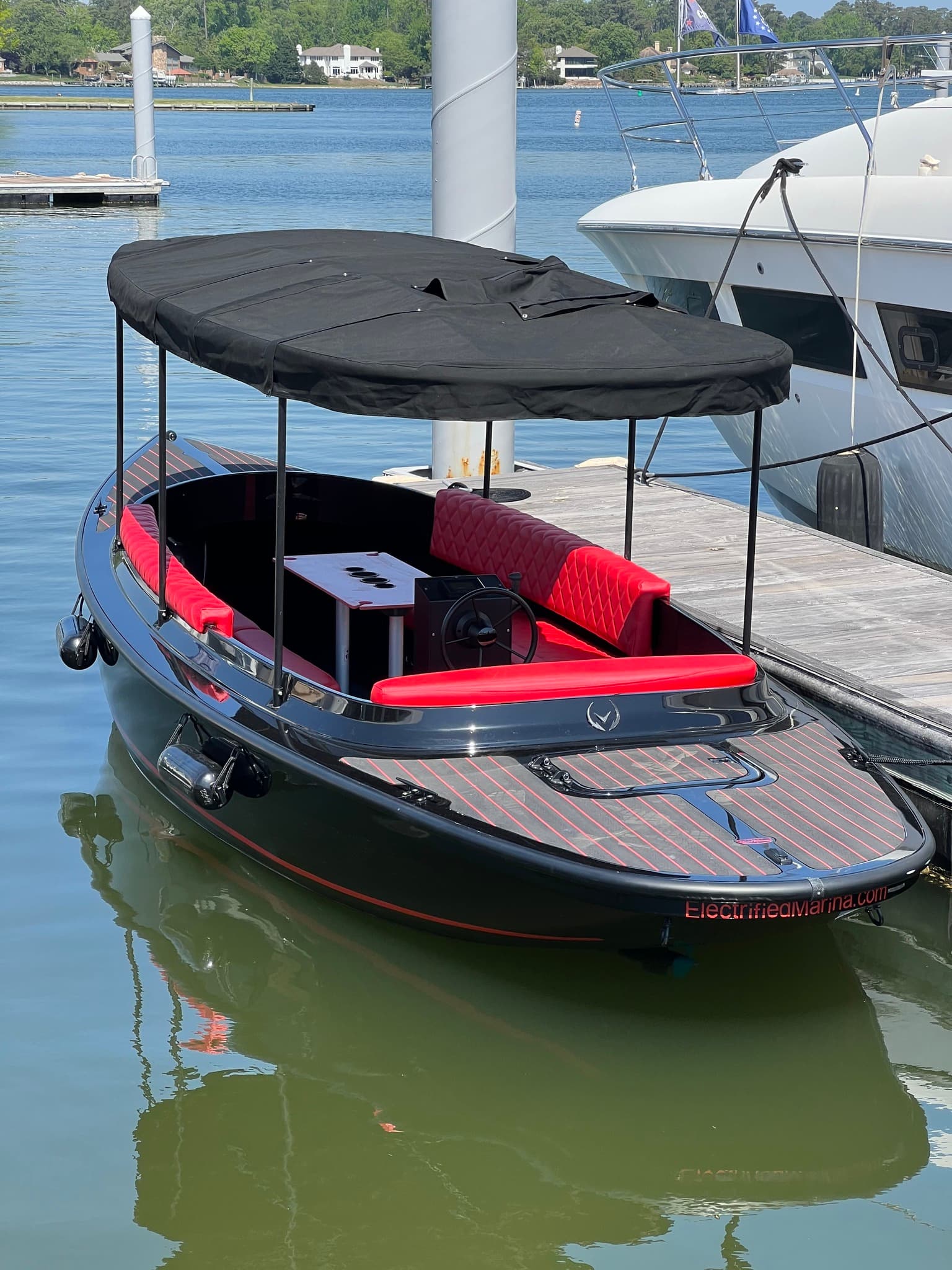 2024 Vision Marine Fantail electric boat docked in a marina, with black canopy, red seating, and patterned deck.