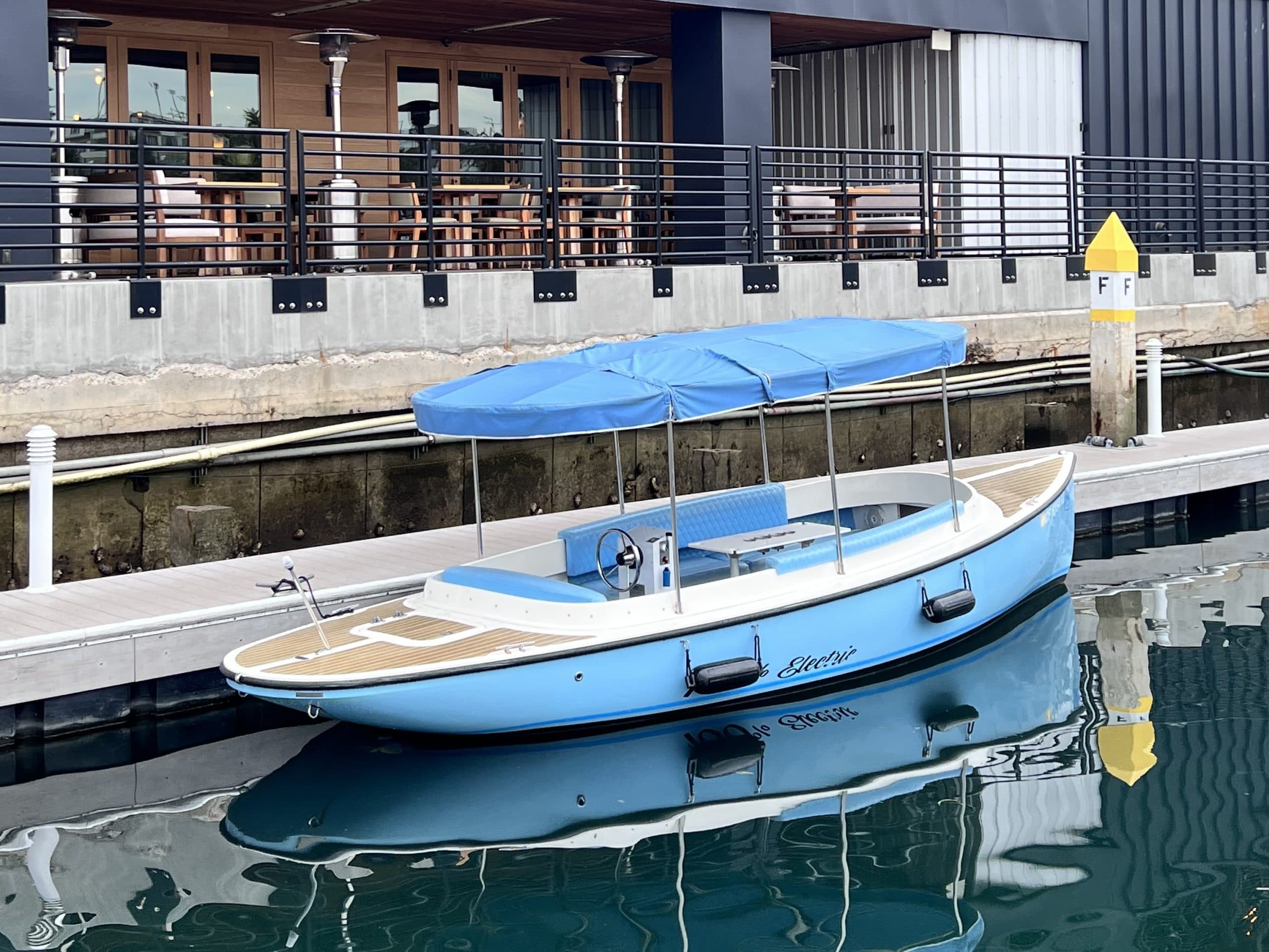 2024 Vision Marine Fantail 217
Light-blue electric fantail boat with a blue canopy moored at a marina dock, with waterfront dining terrace in the background.