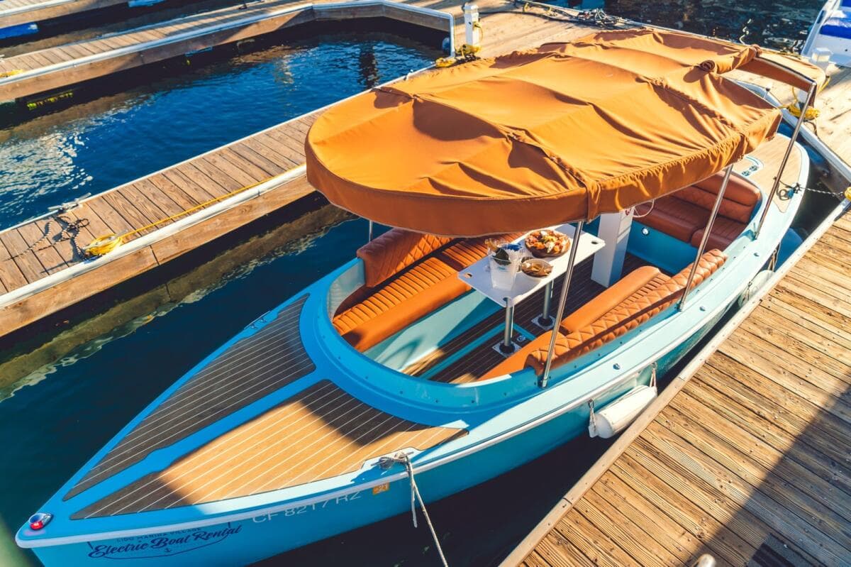 Turquoise Vision Marine Fantail 217 electric boat with orange canopy and seating docked beside a wooden marina walkway.