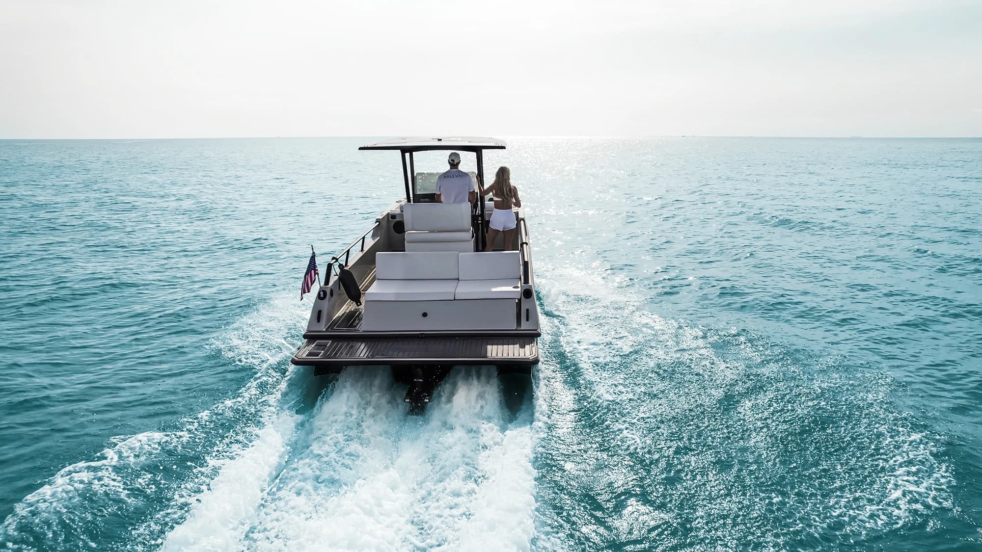 Halevai model2050 electric boat cruising away across open water, viewed from behind with at least two passengers aboard.