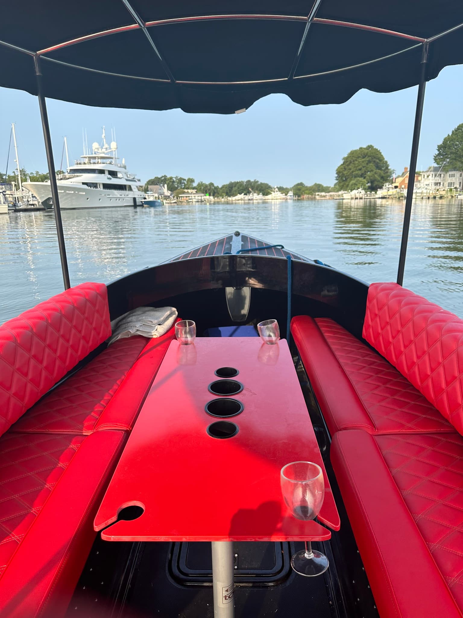 Red quick  upholstered cockpit with a glossy red table with drink holders in the middle, viewed from the helm of a Vision Marine Fantail on calm waterfront with yacht ahead.