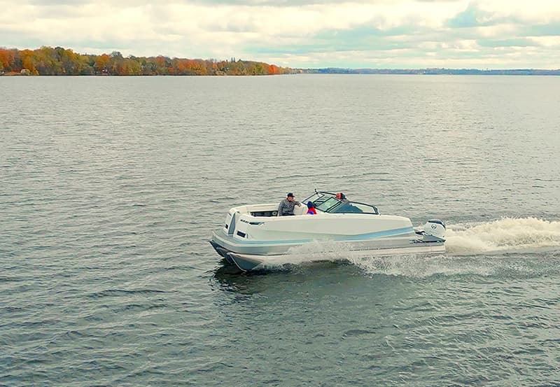 White Vision Marine SPECTR boat cruising across a lake with two people on board, viewed from above and the side with autumn shoreline in the background.