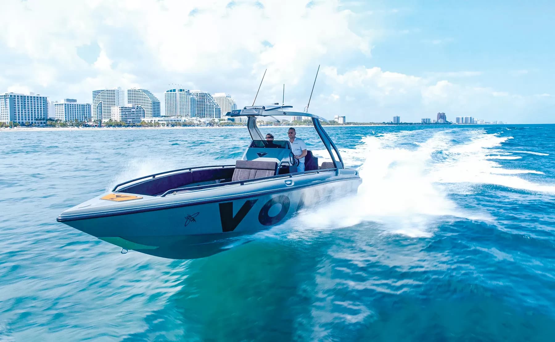 Voltari 260E center-console boat speeding across turquoise water, with a wake and waterfront high-rises in the background.