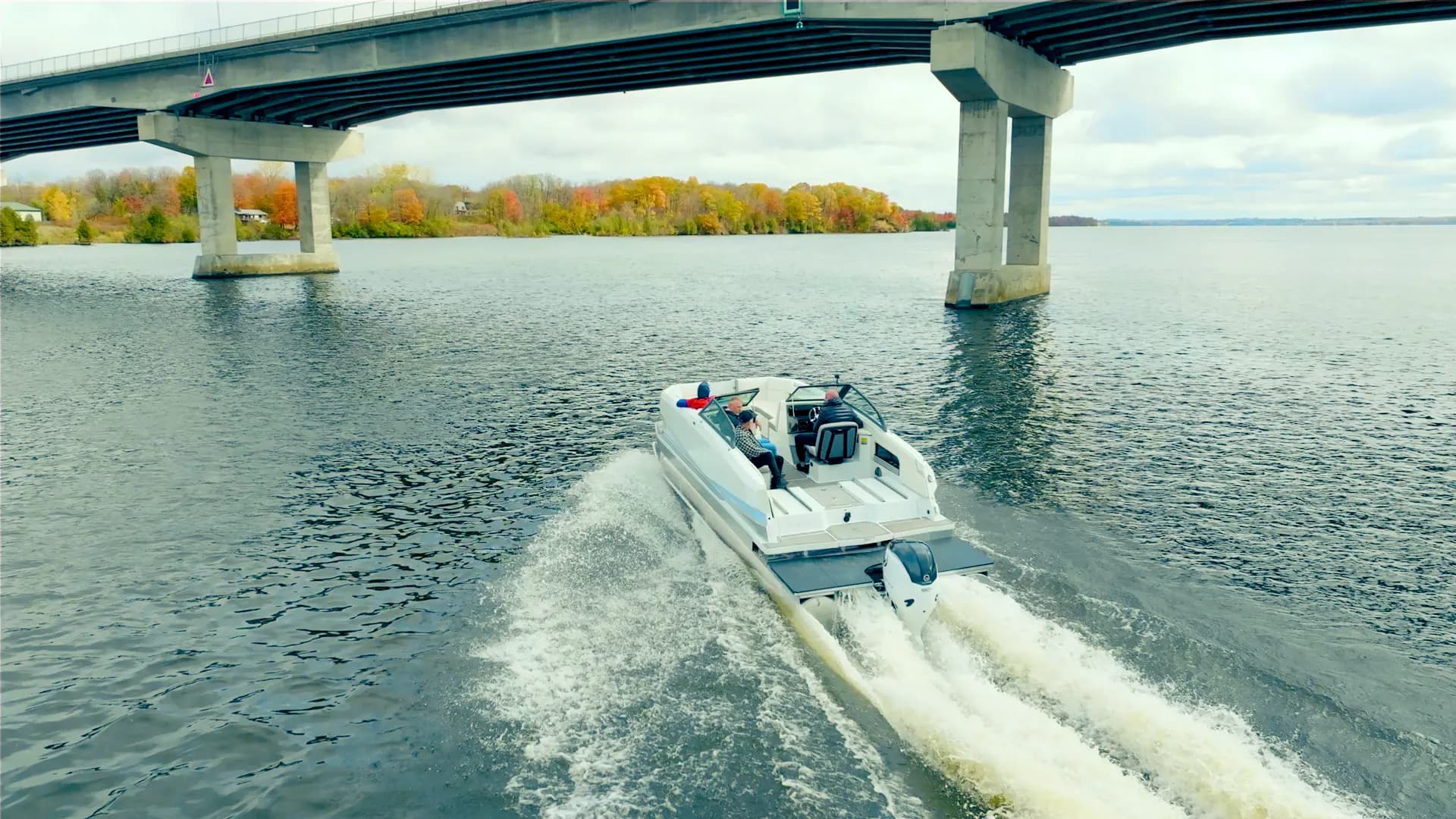 Vision Marine SPECTR powerboat cruising beneath a bridge, viewed from behind on a lake with autumn trees along the shore.
