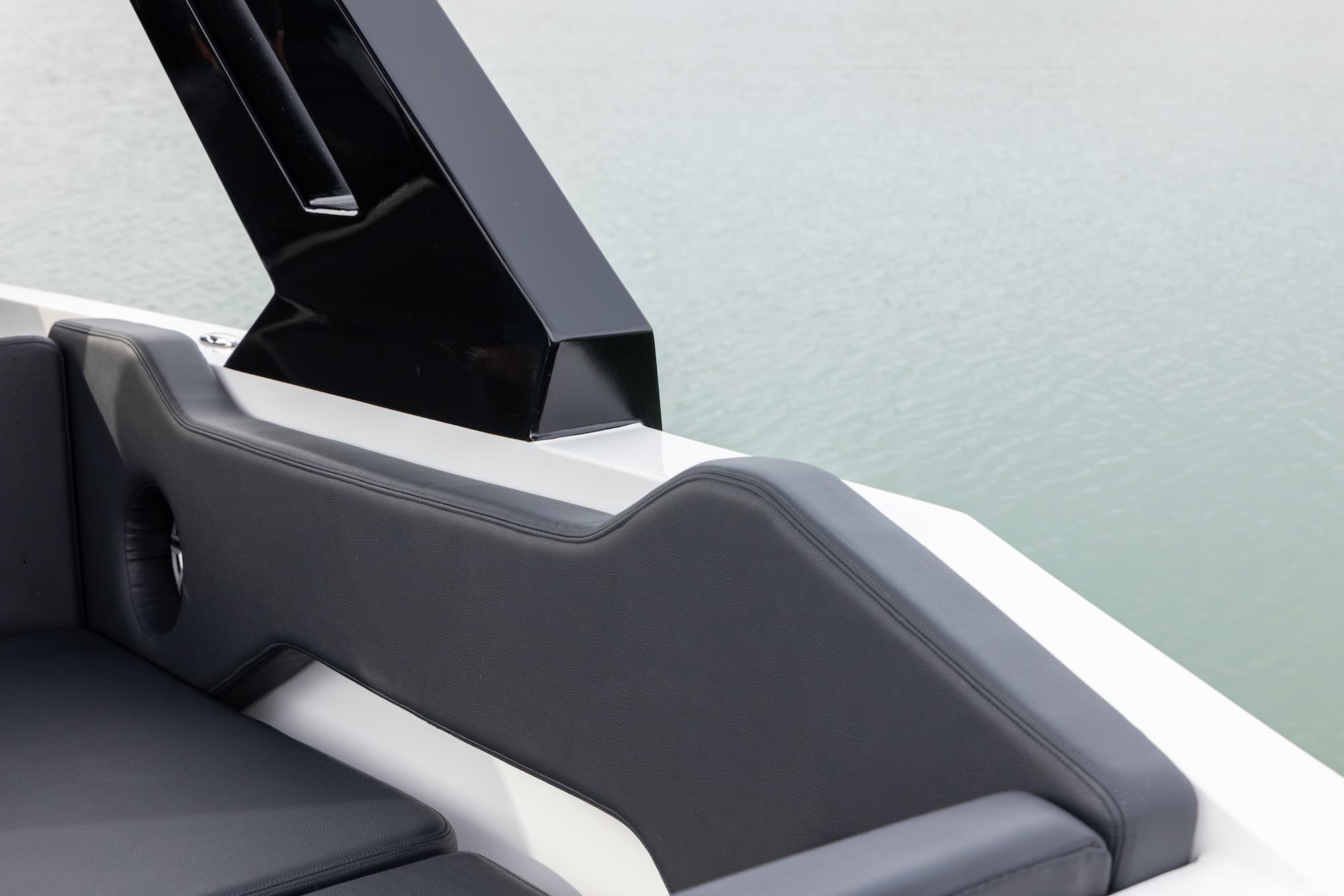 Close-up of a black upholstered boat seat and angular side structure beside the white hull, with calm water in the background (2026 Voltaic AEW24).