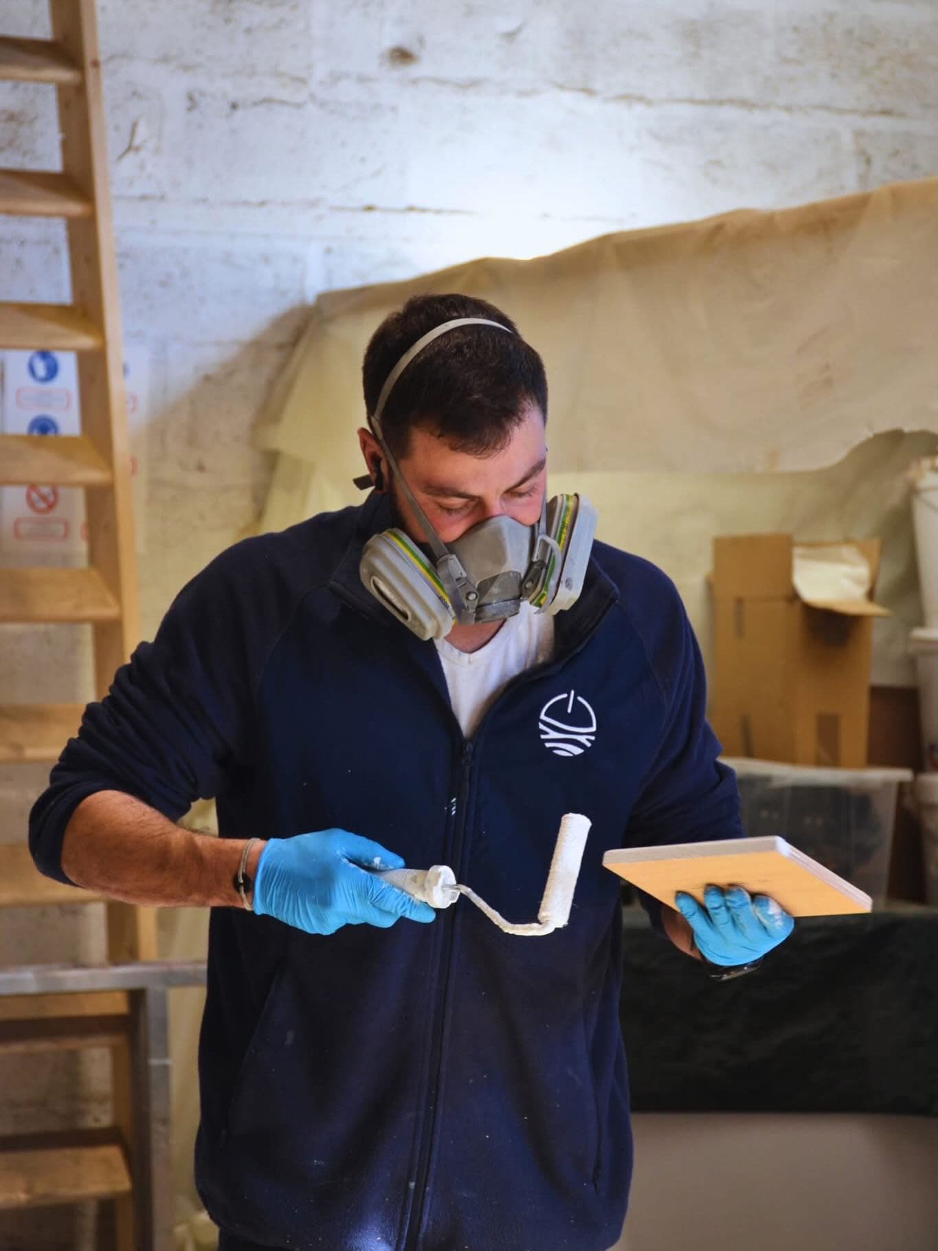 Millikan Worker wearing a respirator and gloves applies coating to a board in a workshop.