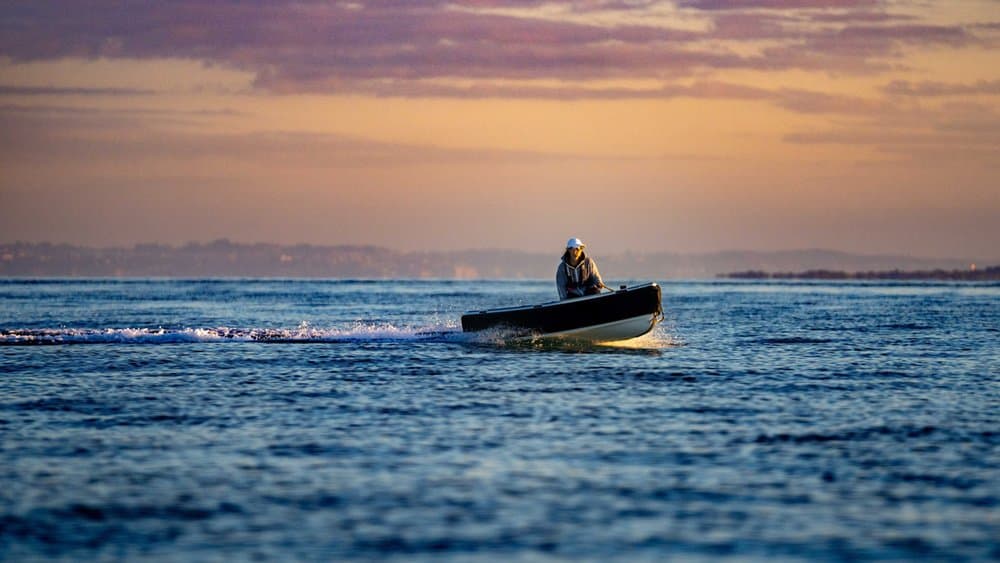 Small open 2026 Offshore Cruising Tenders OC300
 underway on calm water at sunset, viewed from a distance broadside, with one seated person.
