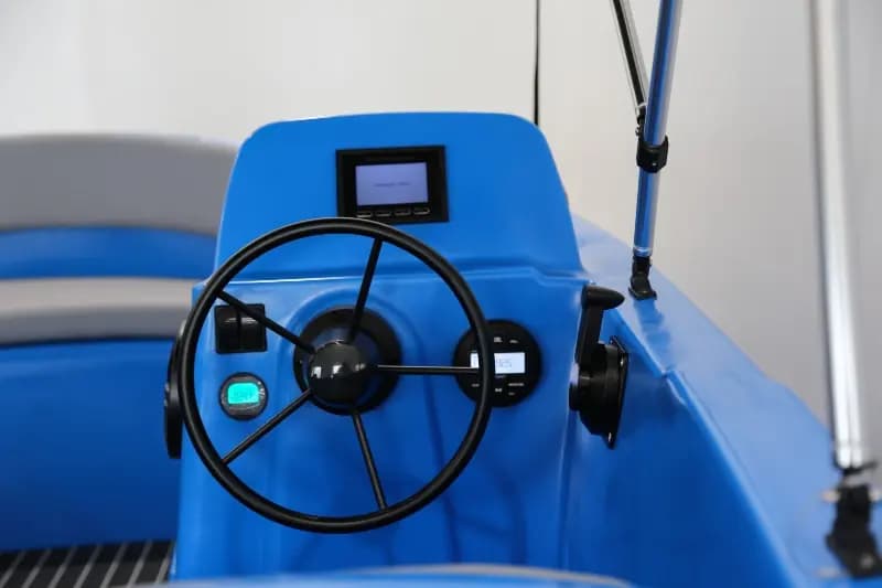Blue electric boat helm with steering wheel, digital display, controls, and throttle mounted on the console.