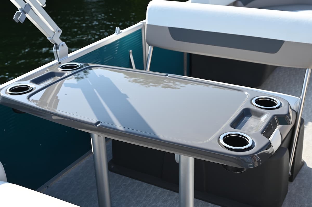 Rear cockpit view of a pontoon boat’s glossy table with four cup holders, beside rear seating and a canopy support (2026 Princecraft Vectra 21 RL).