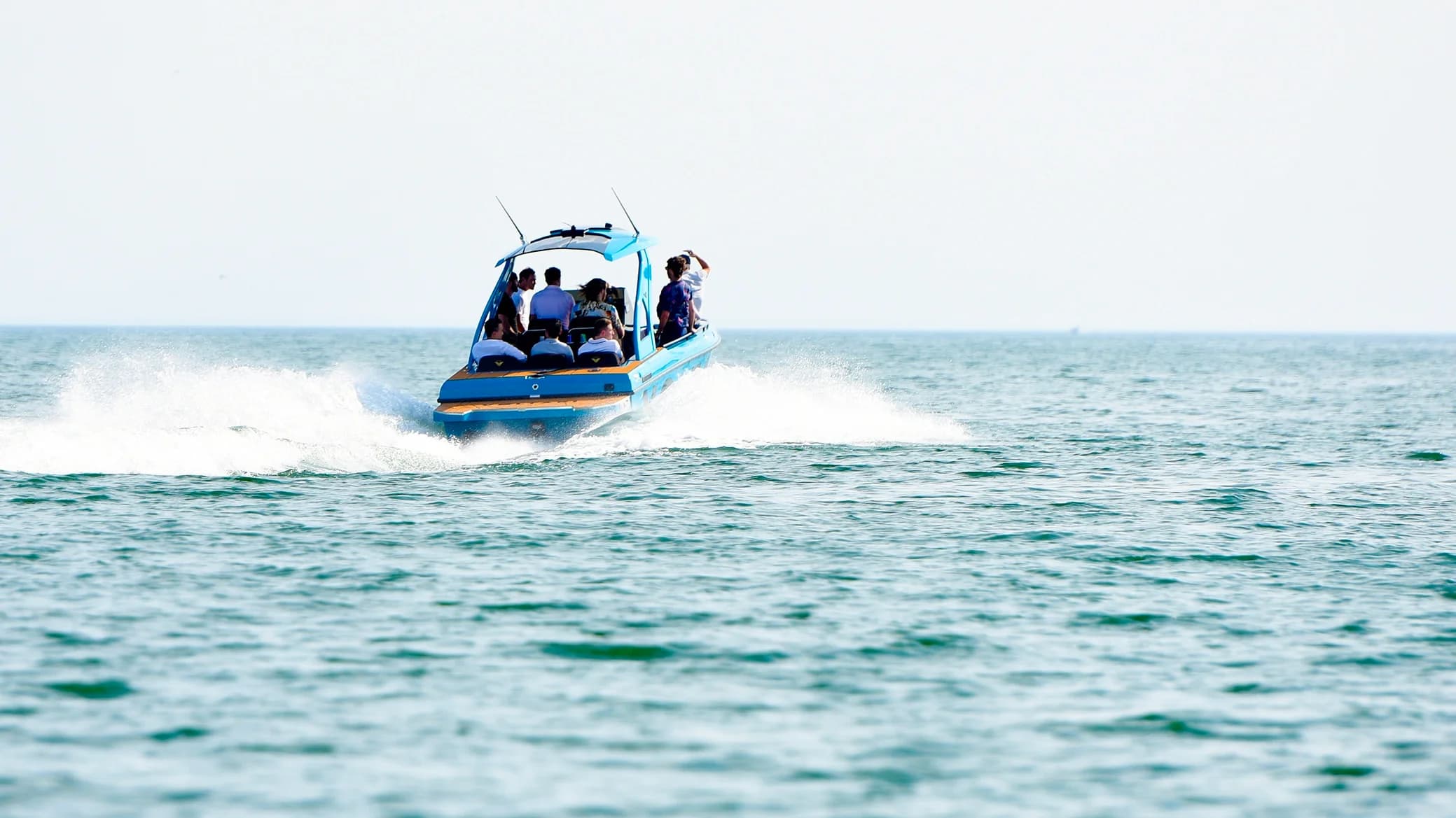 Voltari 260E electric boat speeding across open water with passengers aboard and white wake trailing behind.