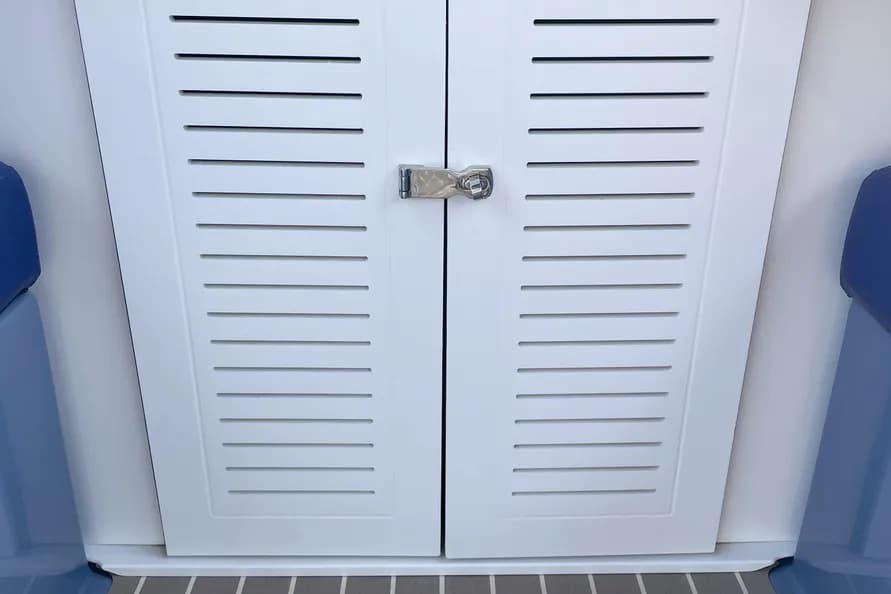 Vision Marine Fantail with white louvered storage cabinet with a central latch inside a boat, flanked by blue seating and a gray nonslip deck.