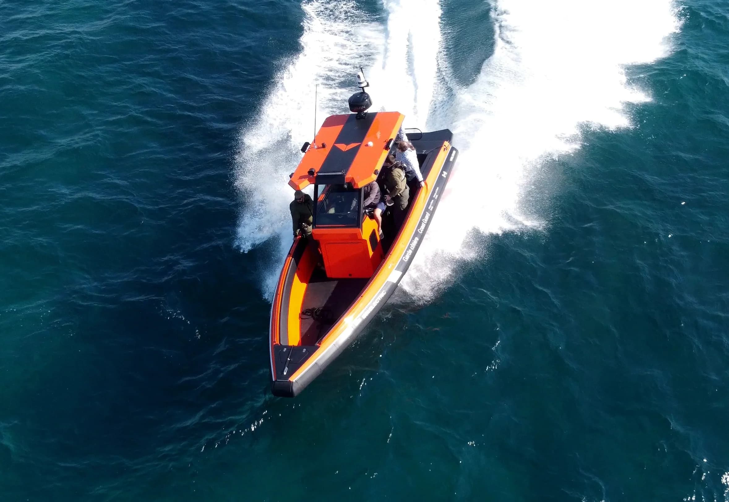 Aerial view of a red-and-orange patrol boat (2026 Voltari Patrol 26) speeding across open water, with its bow in the foreground and a white wake behind.