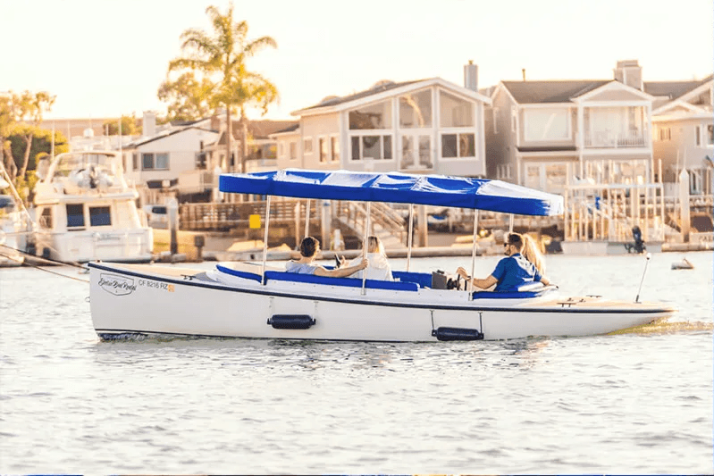 Side view of a white and blue open-deck Vision Marine Fantail with a canopy cruising past waterfront homes.