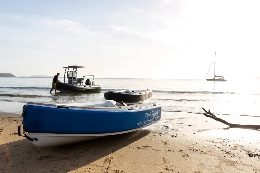 Blue Ocean Cruising Tenders OCT 300 on a sandy beach, with another small boat and a sailboat visible offshore.