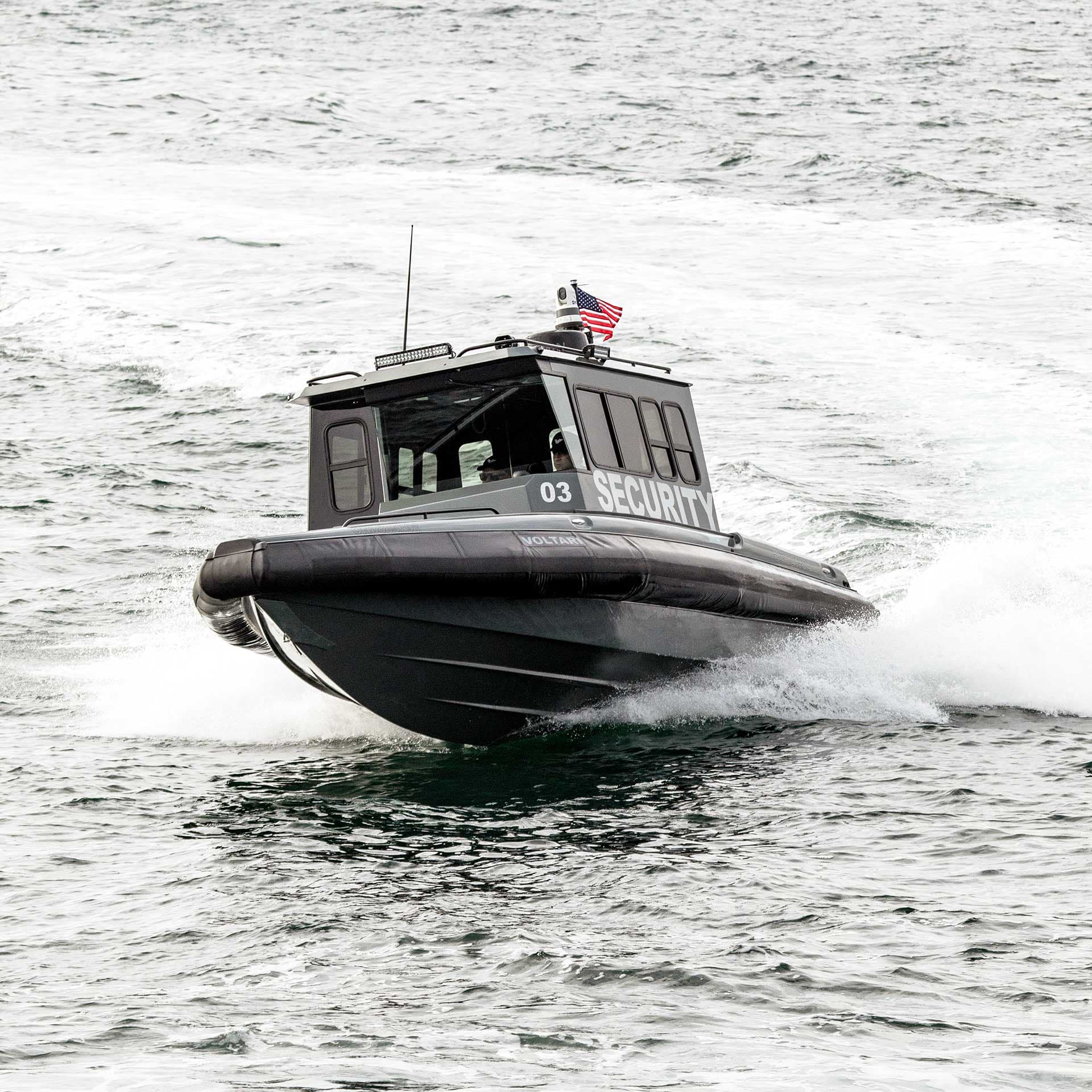 Security-marked patrol boat speeding across choppy water, viewed from the front-left, with a covered cabin and American flag (2026 Voltari Patrol 26).