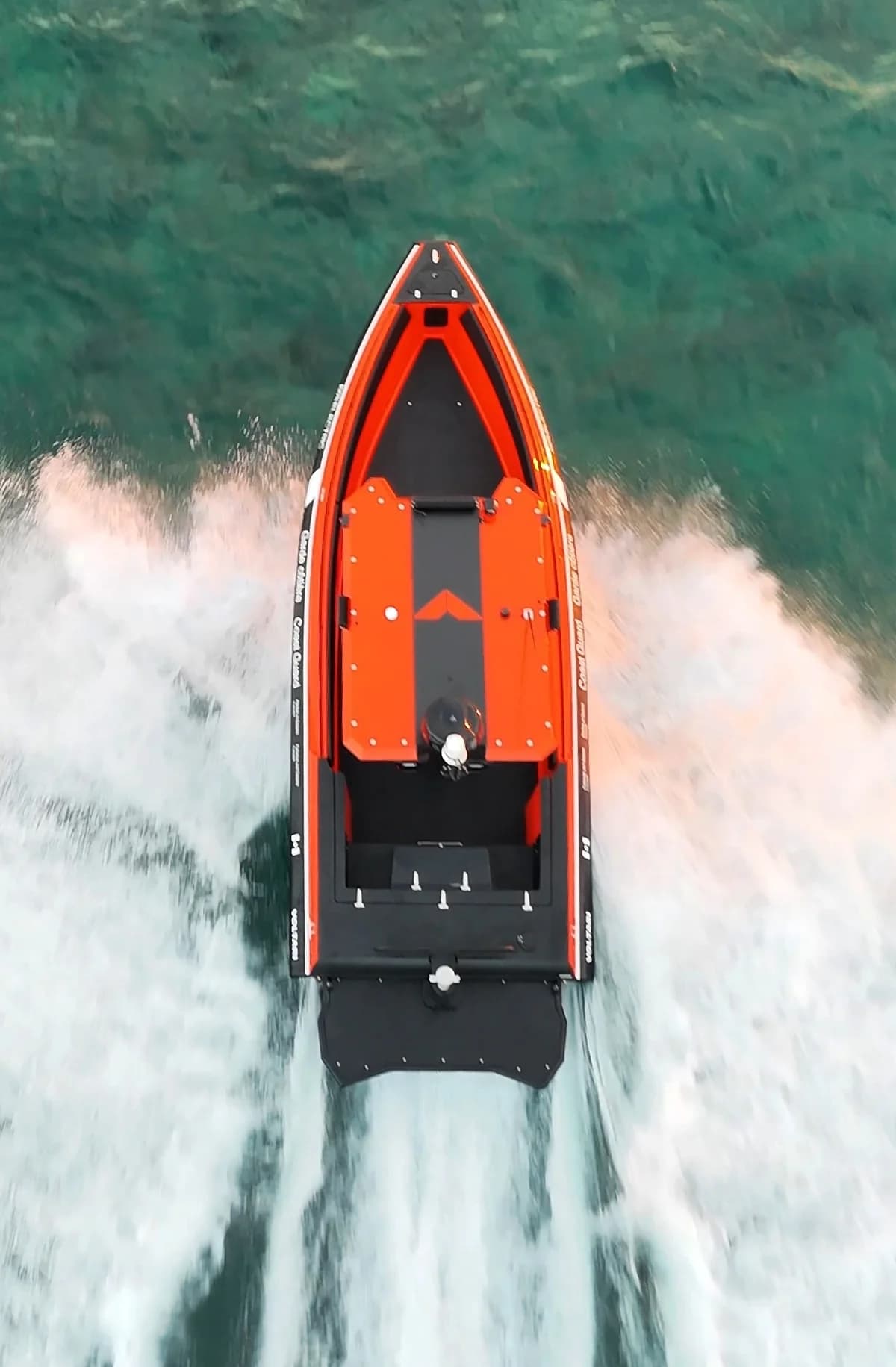 Top-down view of an orange-and-black electric patrol boat speeding through open water, leaving a broad white wake (2026 Voltari Patrol 26)