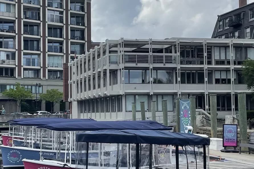 Vision Marina Fantail 217 Covered electric tour boat docked along an urban waterfront, with modern buildings and a public pier in the background.