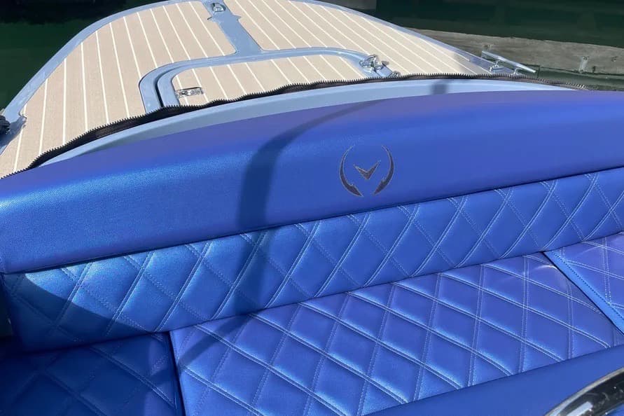 Vision Marine Fantail Blue quilted seating and side panel with a centered emblem on a boat, with the bow deck and water visible beyond.
