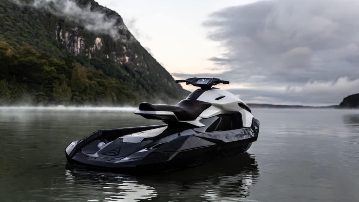 Taiga Orca Performance electric personal watercraft floating on a calm mountain lake beneath misty cliffs and overcast skies.