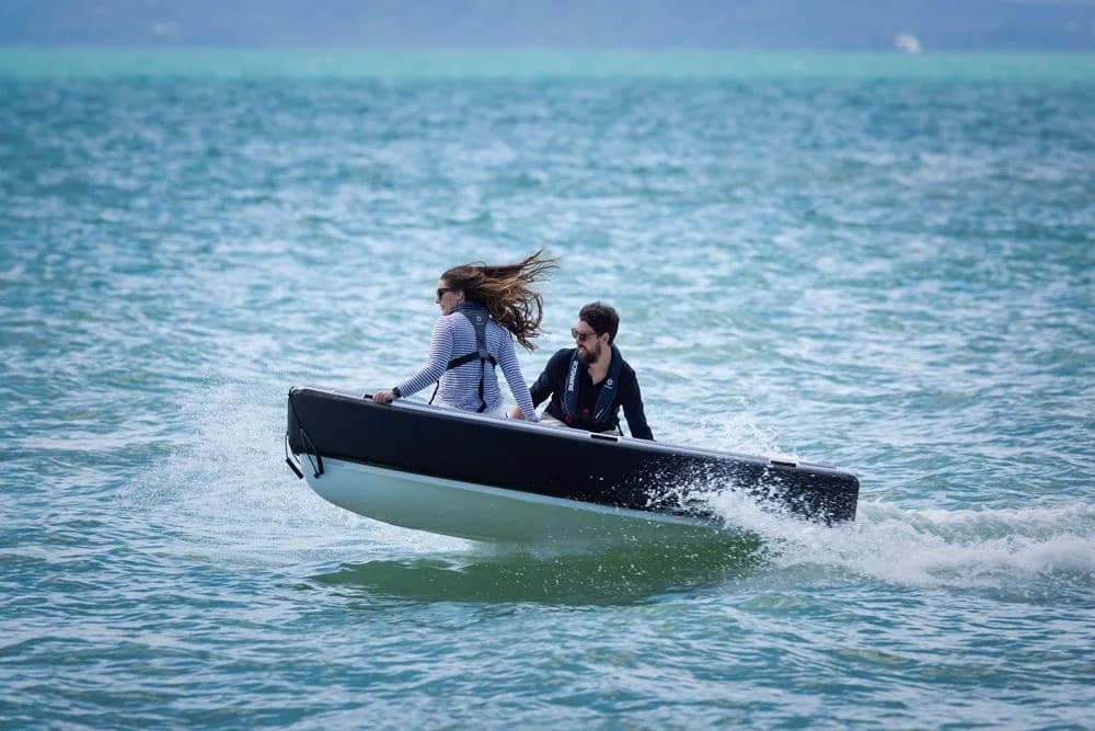 (Offshore Cruising Tenders OC300) Two people going top speed on tender with black rub rail around boat. Boat is planning and coming out of water
