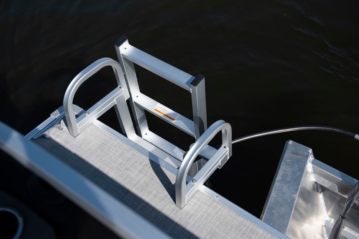 Close-up from above of a 2026 Princecraft Jazz 19 4s swim ladder mounted at the stern platform beside the water.
