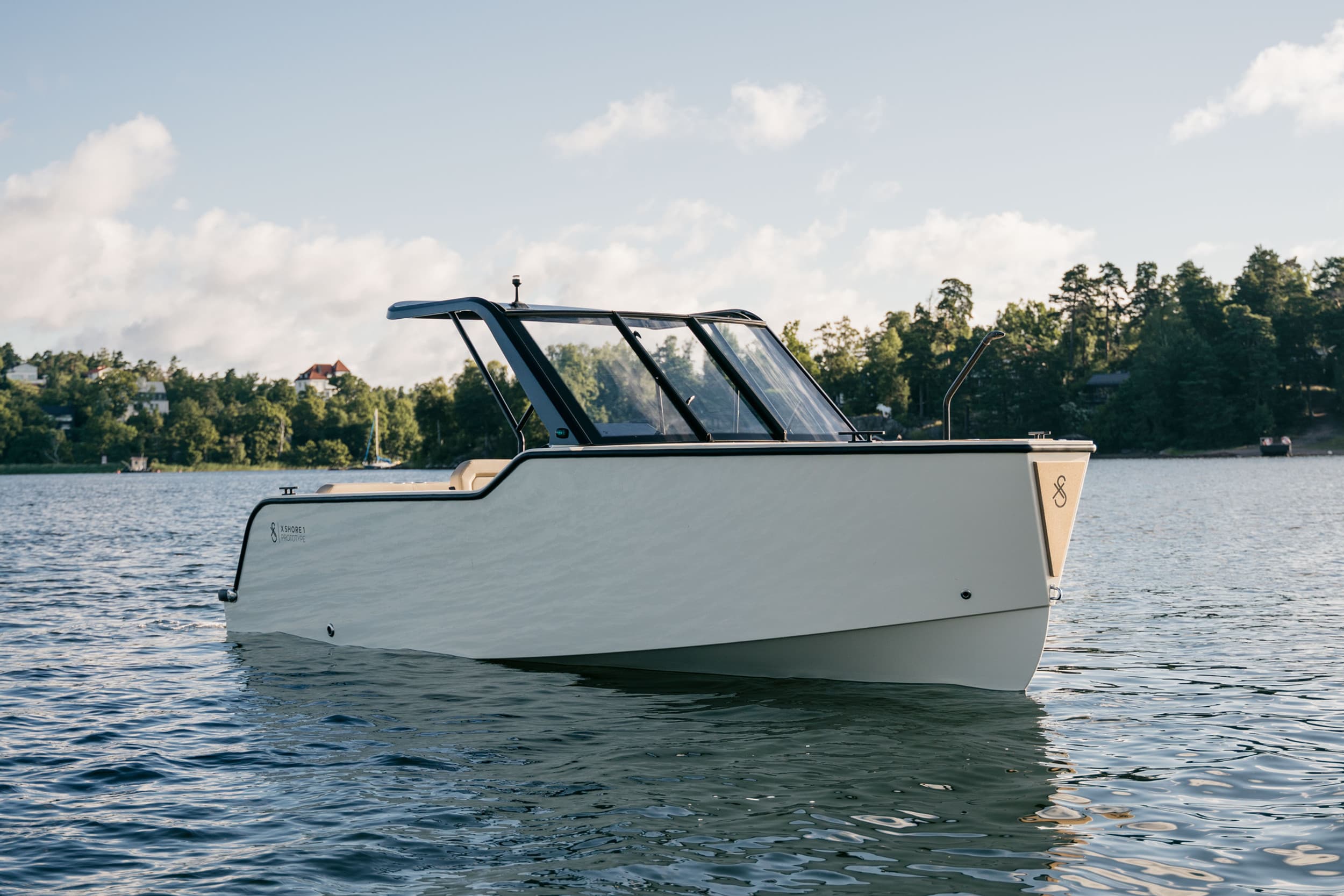 X Shore XS1 viewed from the starboard side on a lake, showing the hull, enclosed windshield, and bow.