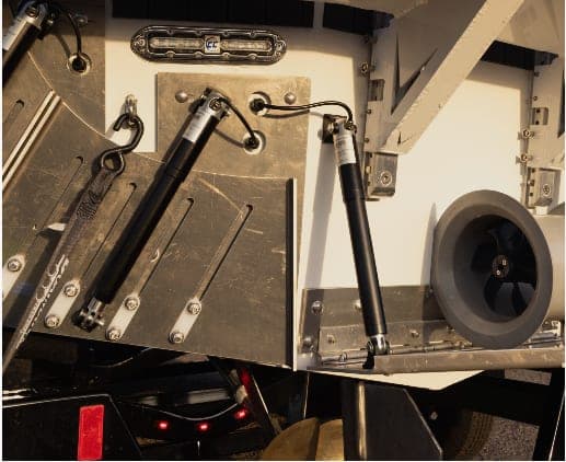 Close-up of boat (2026 Voltaic AEW24) stern hardware, showing two gas struts, mounting plates, wiring, and a round thruster or propeller housing.