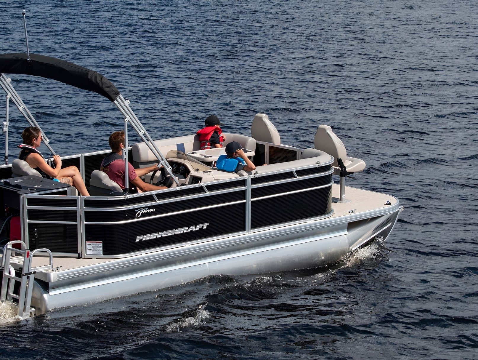 Princecraft Jazz 19 4s pontoon boat underway, viewed from the side with the bow to the right and passengers seated in the cockpit.
