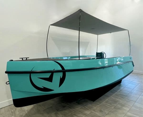 Vision Marine Volt 180 viewed from the front-left side, showing the turquoise hull, canopy, and bow logo indoors.