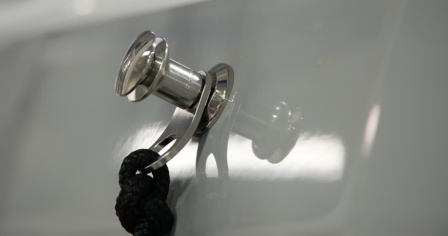 Close-up of a polished metal cleat mounted on a white boat (2026 Vision Marine SPECTR) surface, with a black braided line attached.